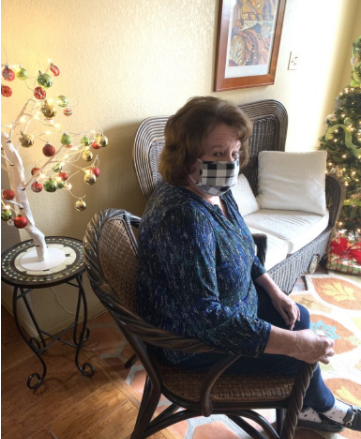 The authors grandmother in a chair in a house while wearing a mask. Not all individuals are able to work from home, which could put them and their families at risk of COVID-19. This danger will last longer if essential workers are not prioritized as one of the first groups to get the vaccine.